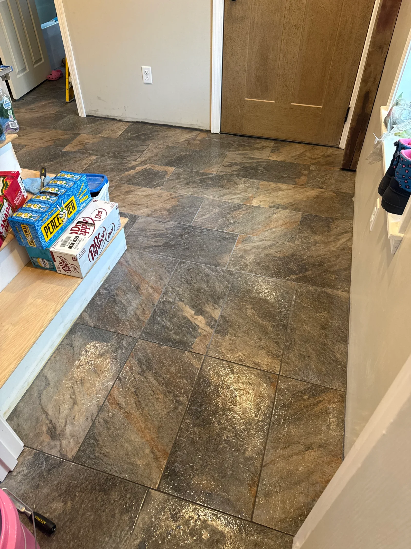 Large-format slate-look tile floor with narrow grout lines in an entryway, transitioning to a wood step and white baseboard