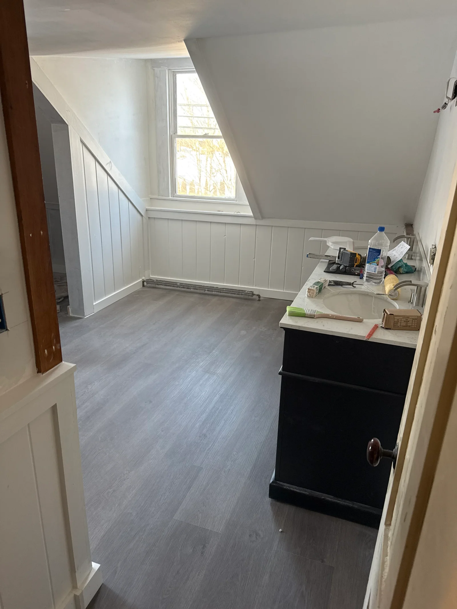 Attic bathroom with gray vinyl plank flooring, white vertical wainscoting, and dark vanity with quartz countertop and undermount sink