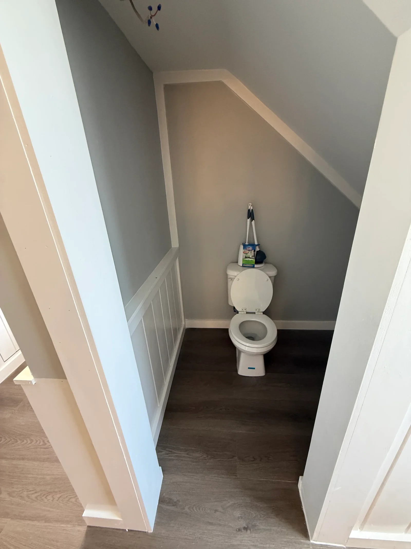 Under-stair powder room with white board-and-batten wainscoting, gray painted walls, and dark wood-look vinyl plank flooring