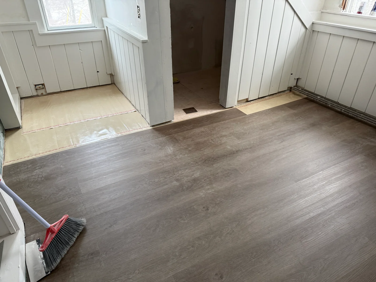 Gray-brown wood-look vinyl plank flooring installed over tan underlayment beside white beadboard wainscoting