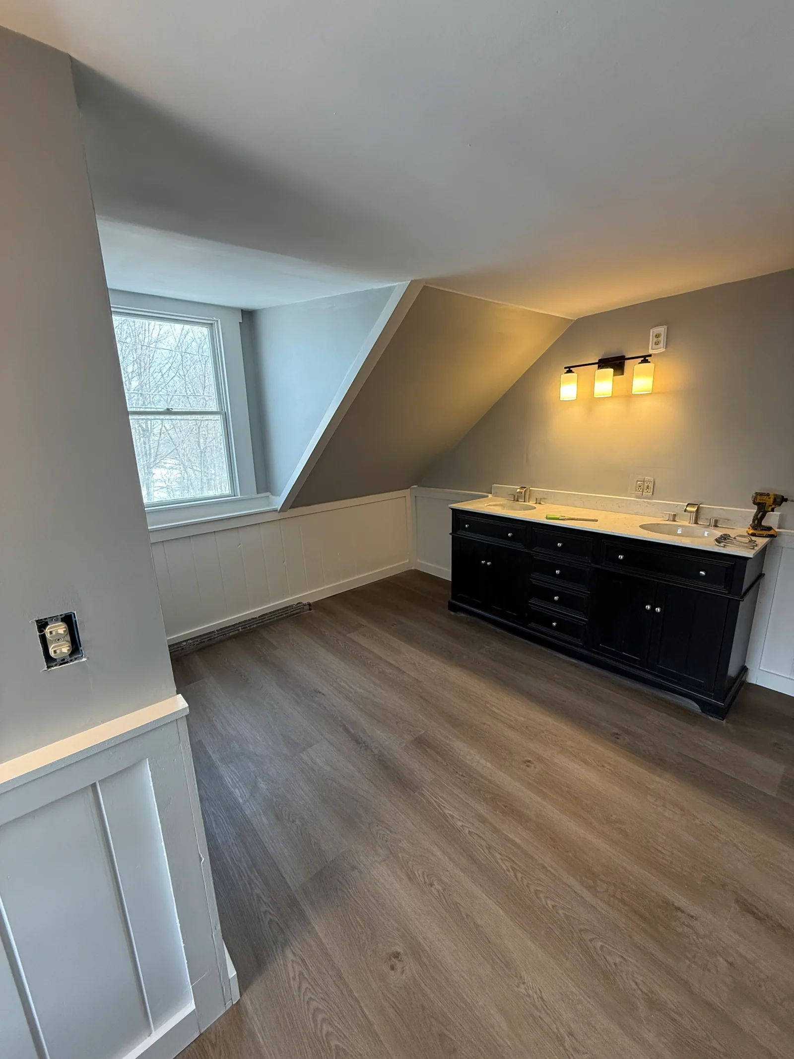 Attic room with black double vanity, quartz countertop, white beadboard wainscoting, and wood-look vinyl plank flooring