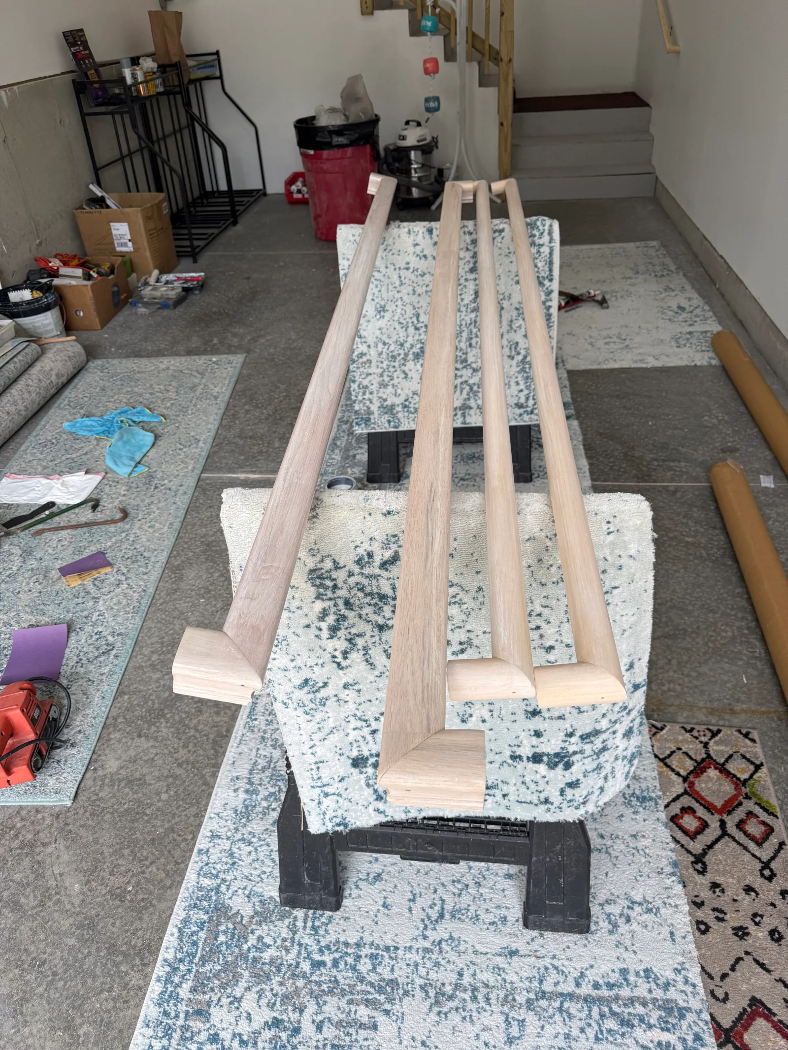 Four unfinished hardwood handrail sections with rounded profiles and mitered end returns resting on sawhorses in a workshop