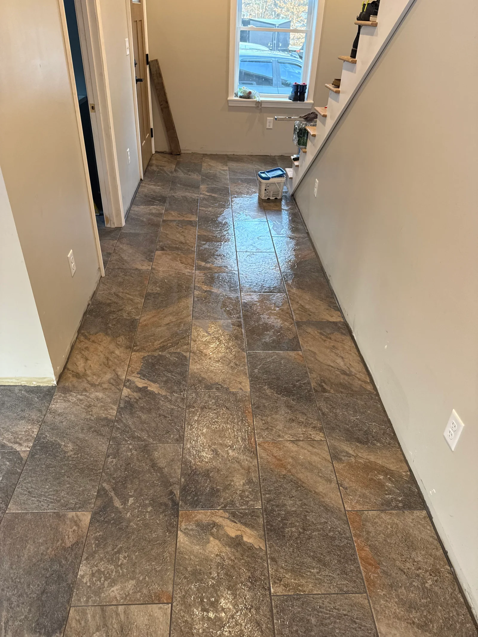 Large-format slate-look porcelain floor tile laid in staggered pattern in hallway beside painted staircase