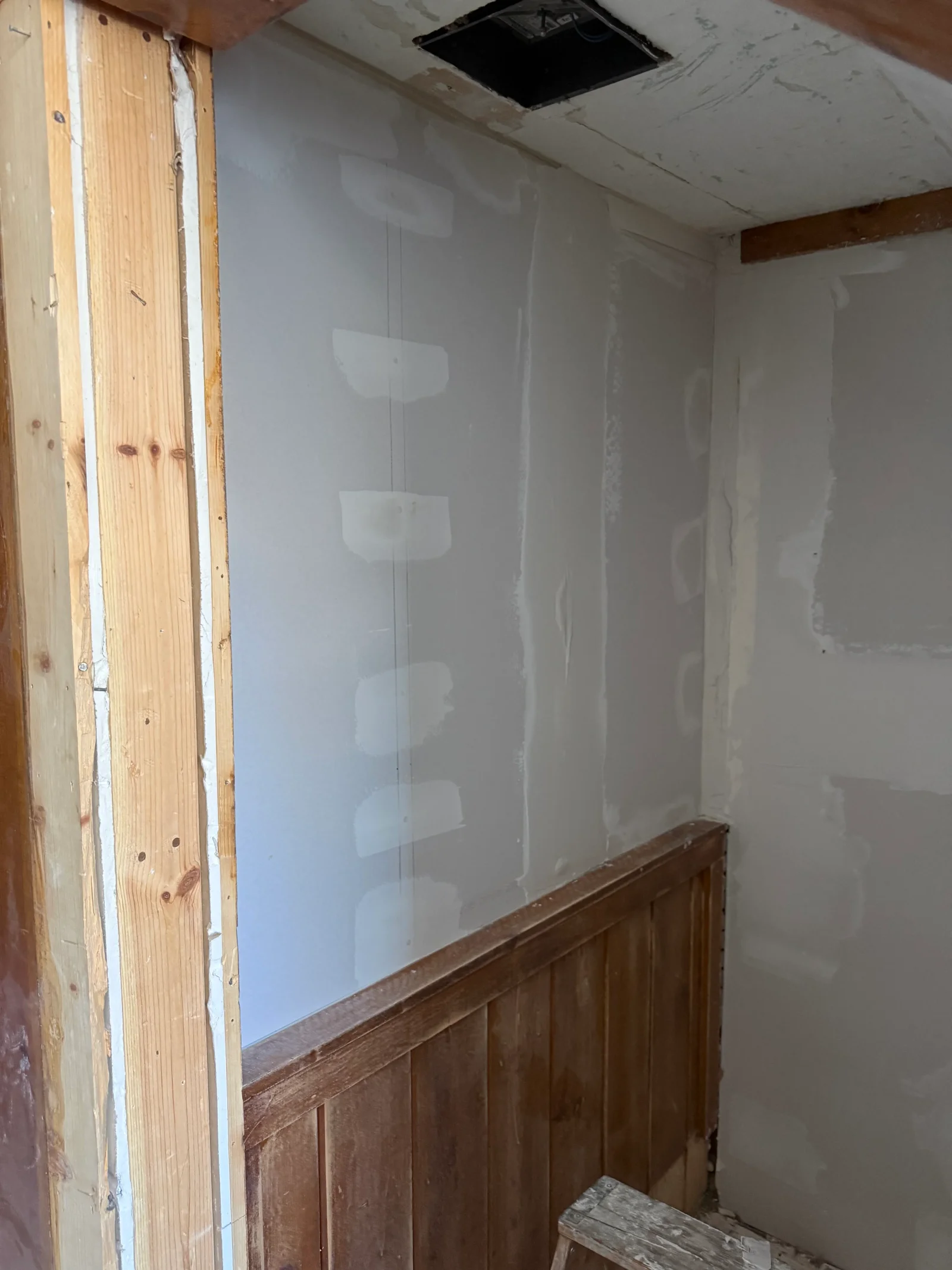 Drywall with joint compound taping in progress over wood wainscot and exposed wood door framing