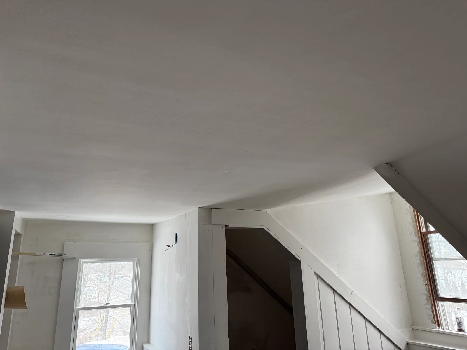 Smooth white plastered ceiling and walls with painted trim and beadboard paneling along a staircase opening
