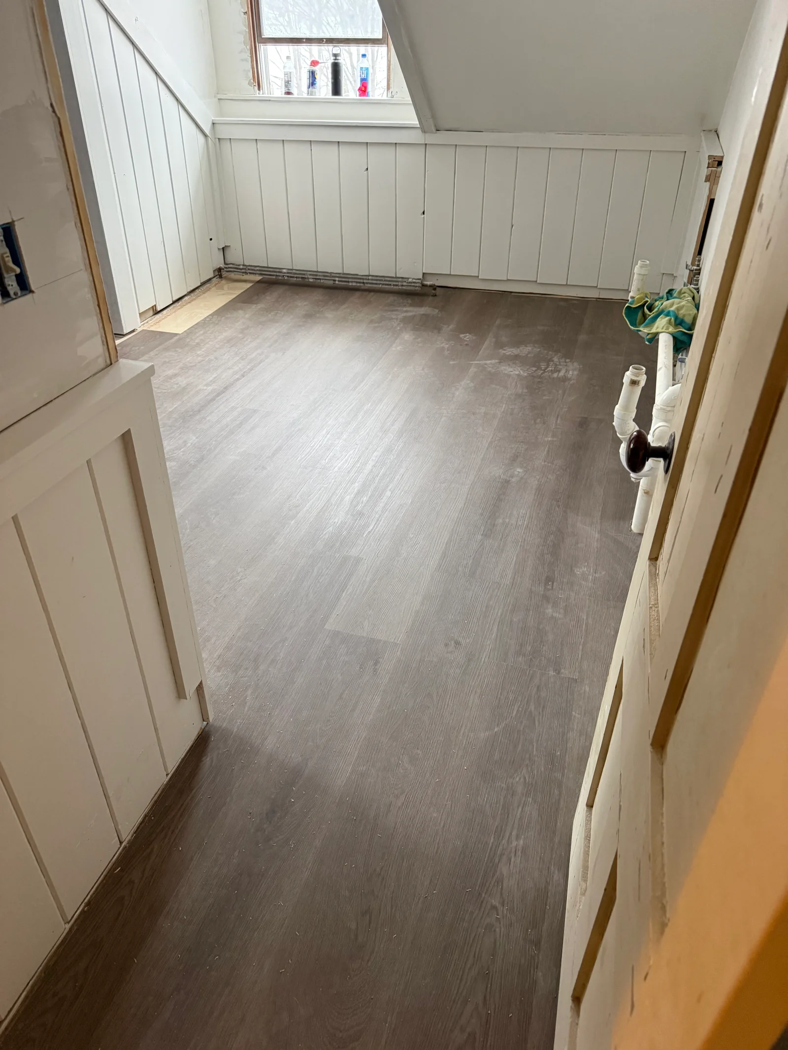 Attic room with gray wood-look vinyl plank flooring, white vertical paneled knee walls, and sloped ceiling