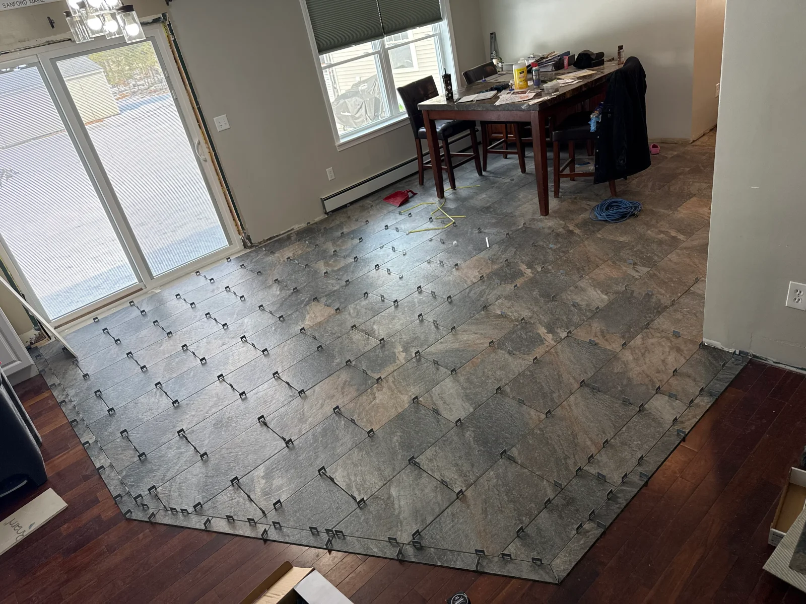 Large-format gray stone-look porcelain floor tiles being laid with leveling clips and spacers over a subfloor