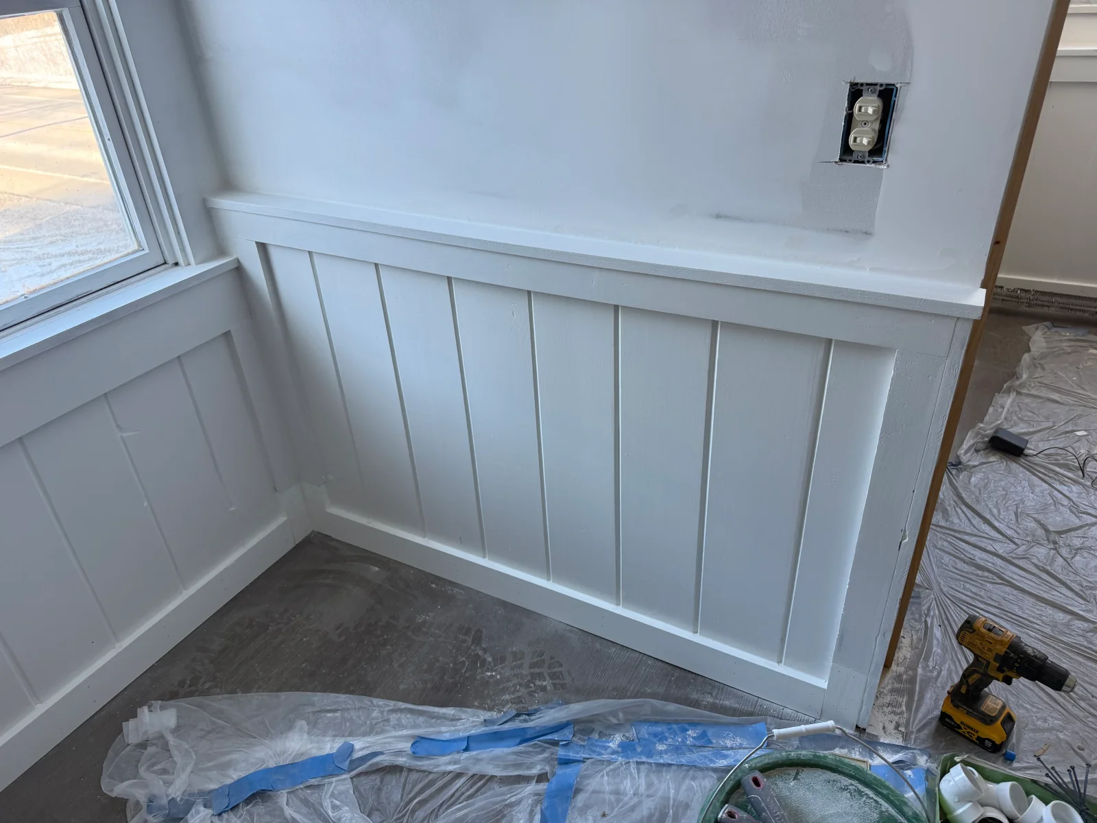White vertical board and batten wainscoting with painted cap rail and base trim beside a window