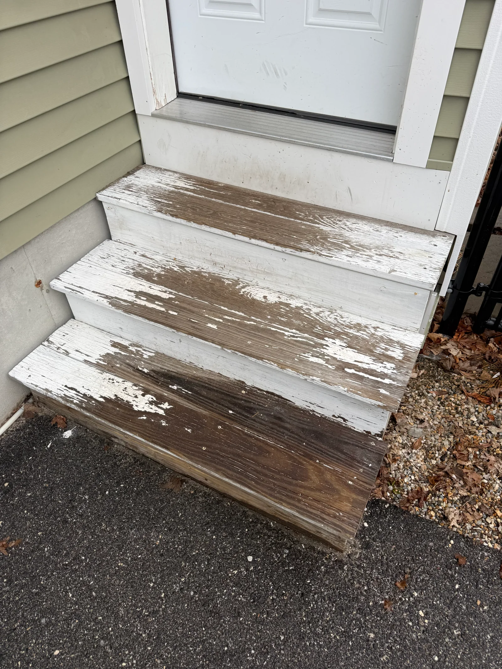 Weathered wood exterior steps with peeling white paint exposing brown wood beneath, leading to a white entry door