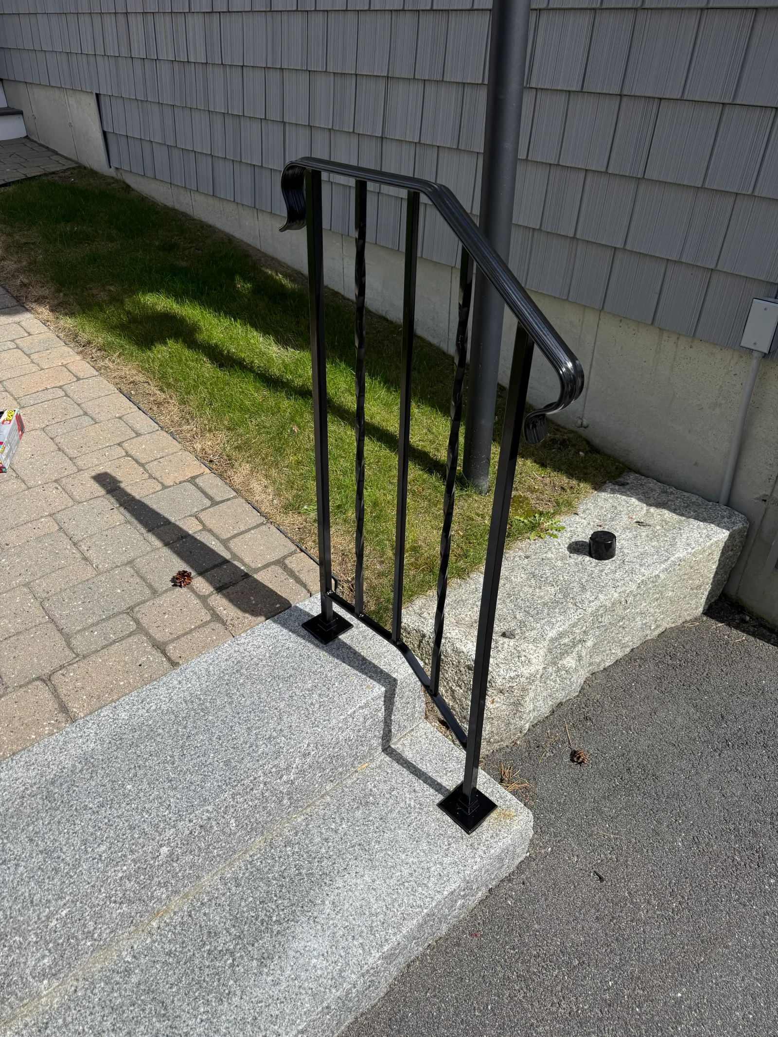 Black steel entry handrail with twisted balusters and square base plates on granite steps