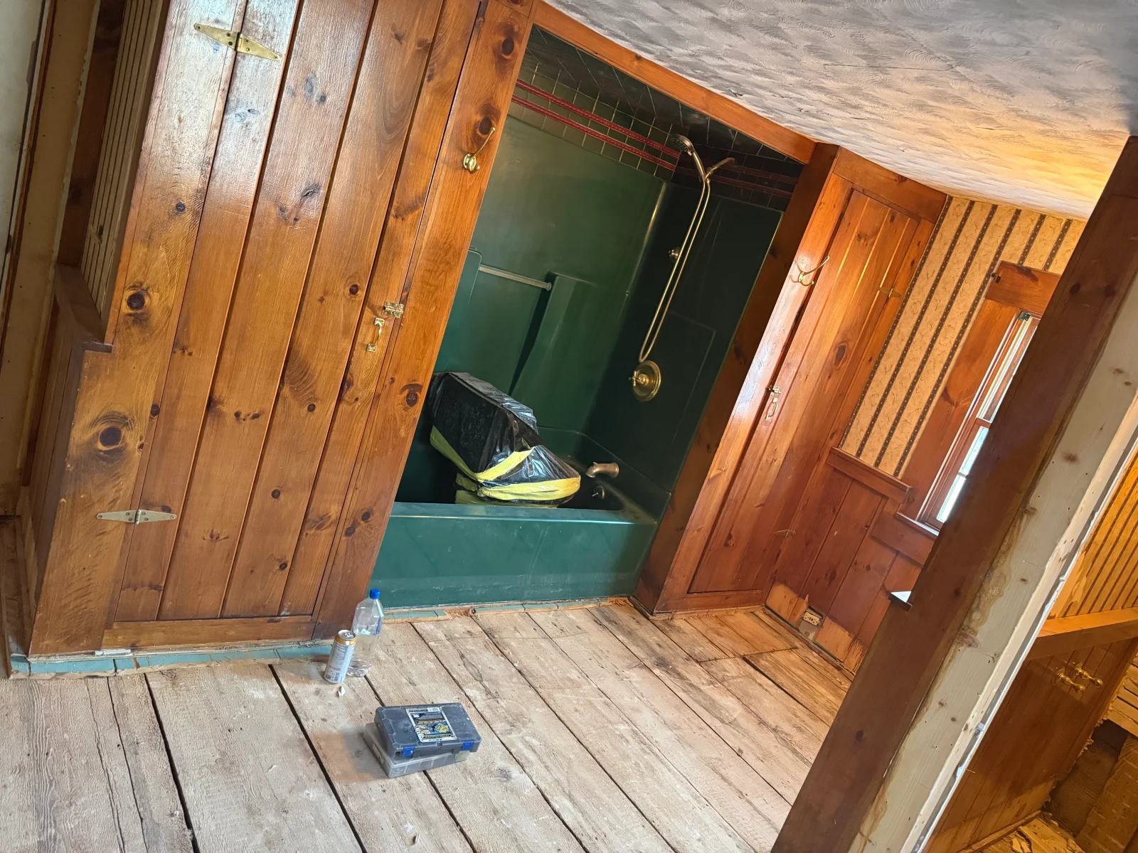 Knotty pine paneling and brass hardware in a bathroom with green tub and wood plank floor